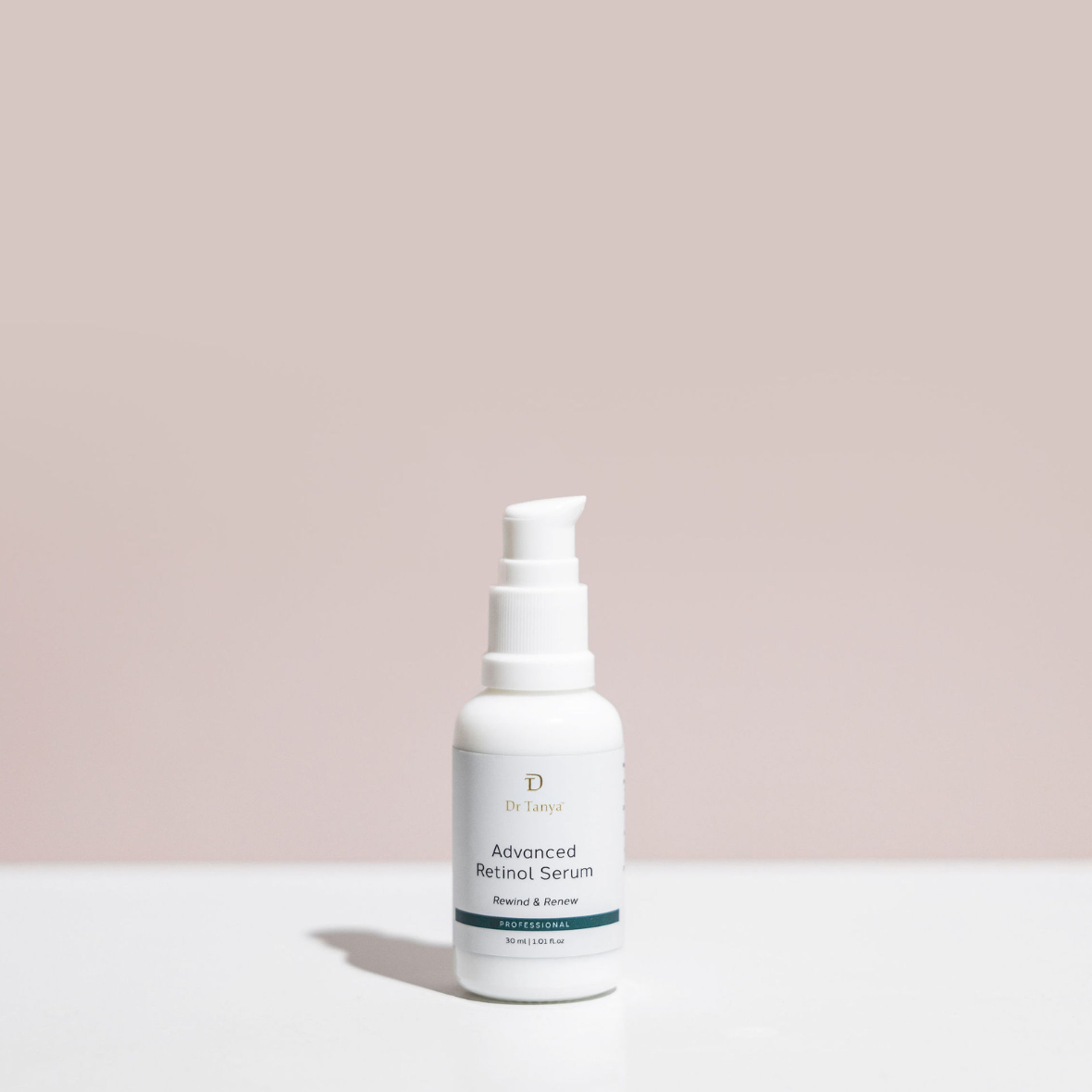 A small white bottle of face serum on a white surface against a pink backdrop