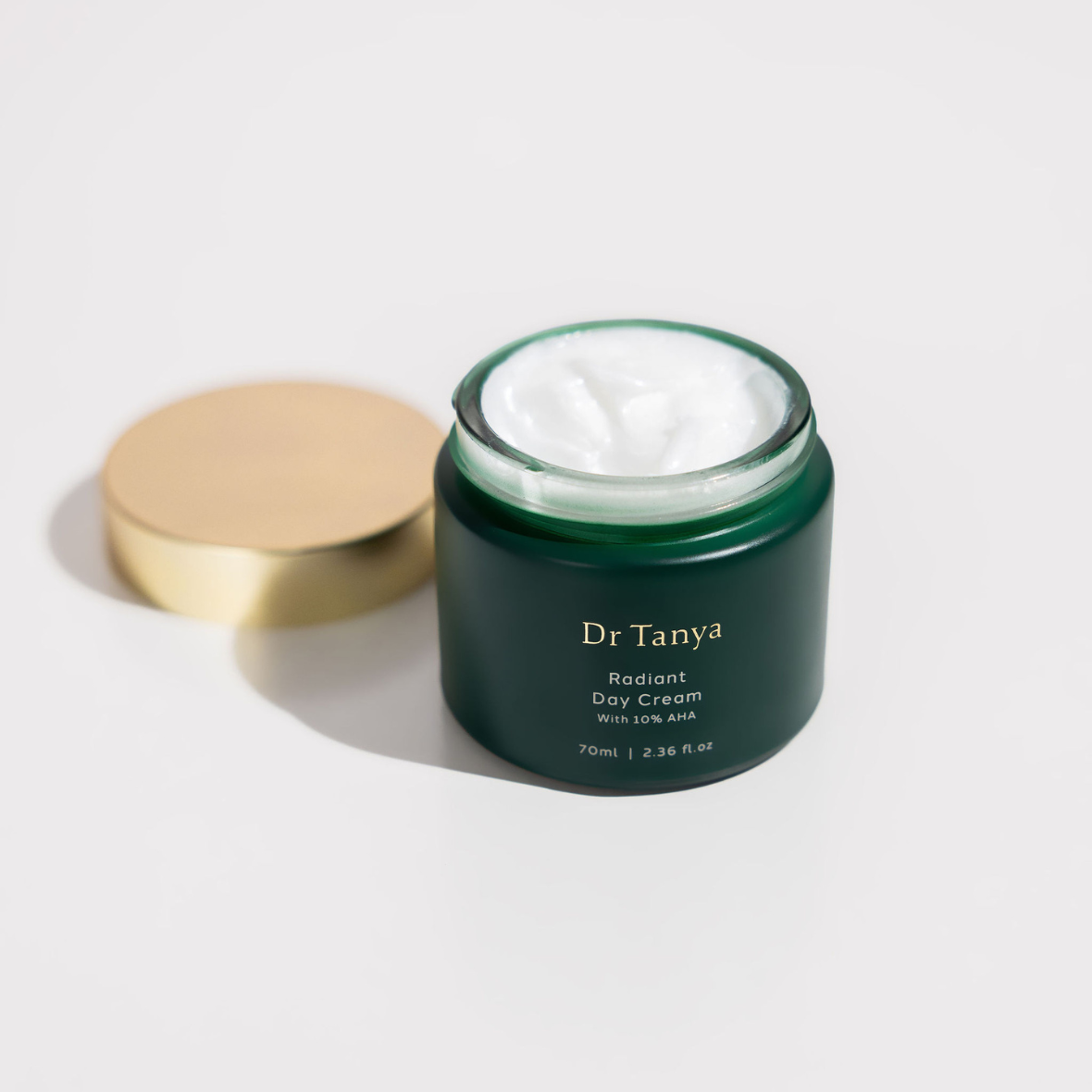 An opened emerald green pot of day cream showing white product inside