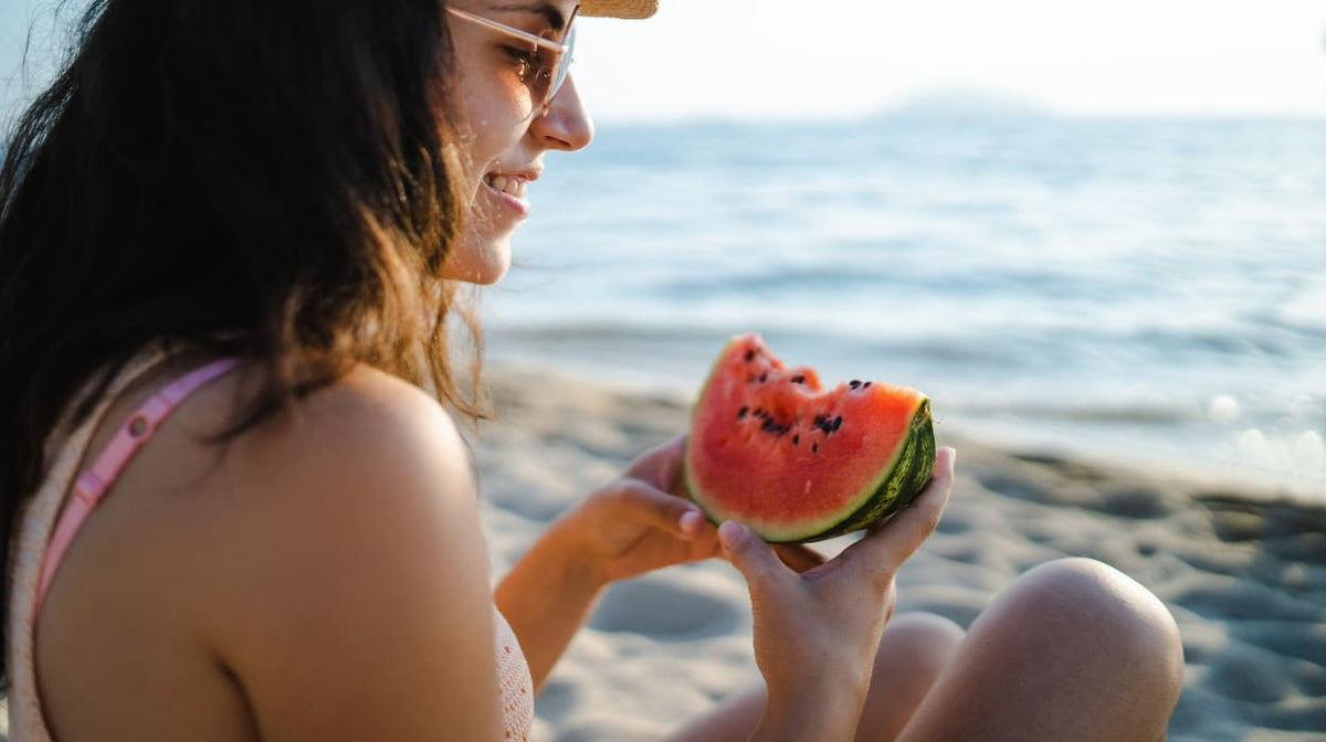 A woman eats watermelon at the beach