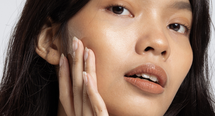 A lady with glowing skin holding her hand to her cheek