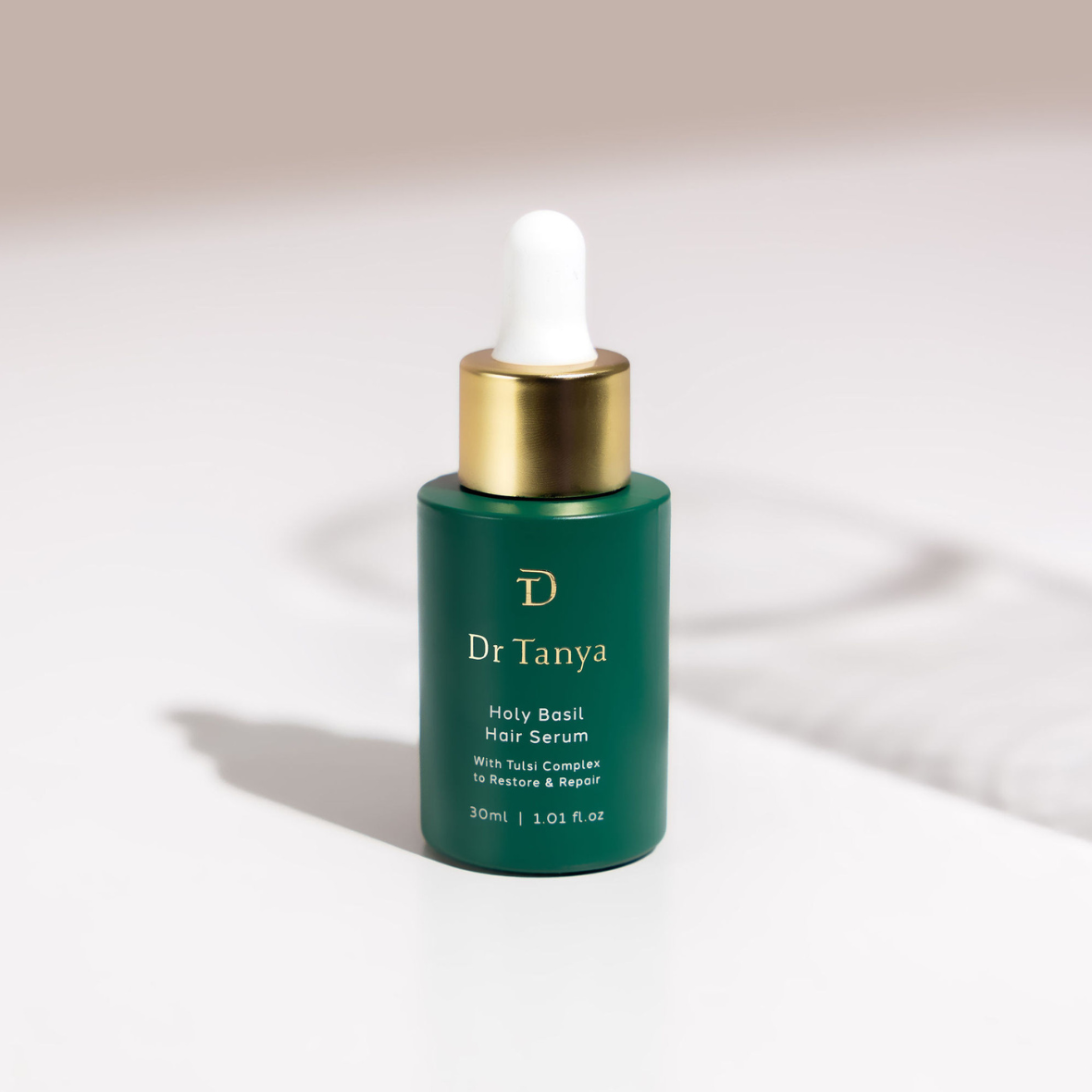 A green bottle of hair serum on a white surface with shadows cast