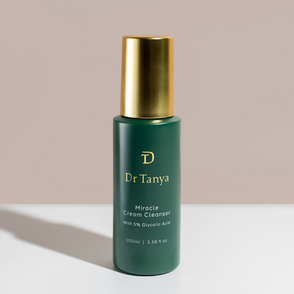 A green and gold bottle of Dr Tanya's miracle cream cleanser in front of a pale pink wall